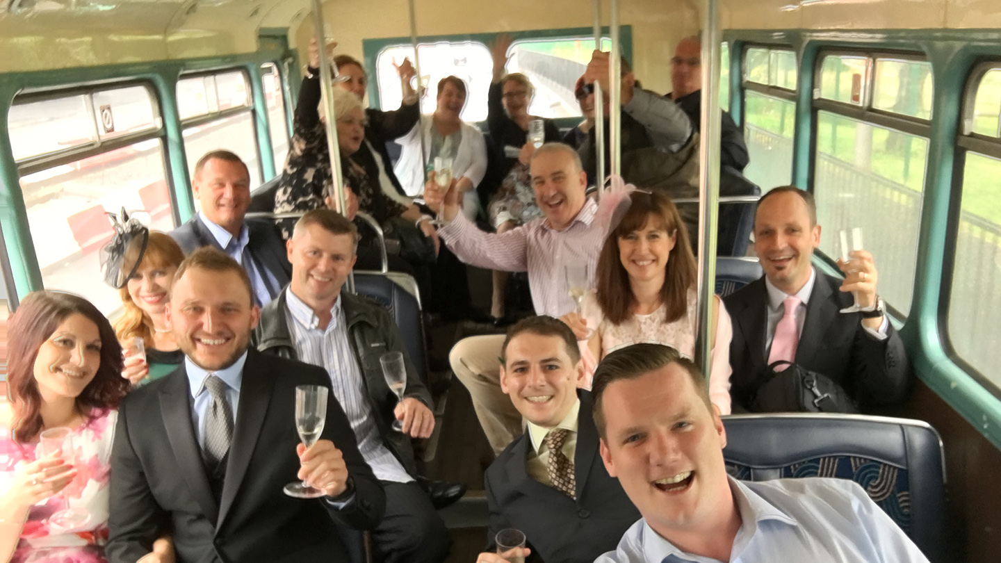 Wedding guests smiling and seated inside the lower deck of a vintage cream Leyland double decker bus.