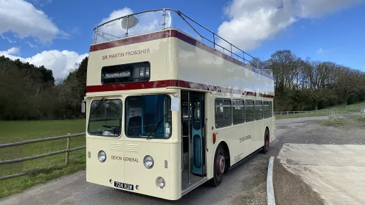 Cream vintage Leyland double decker bus parked beside farmland and countryside scenery.