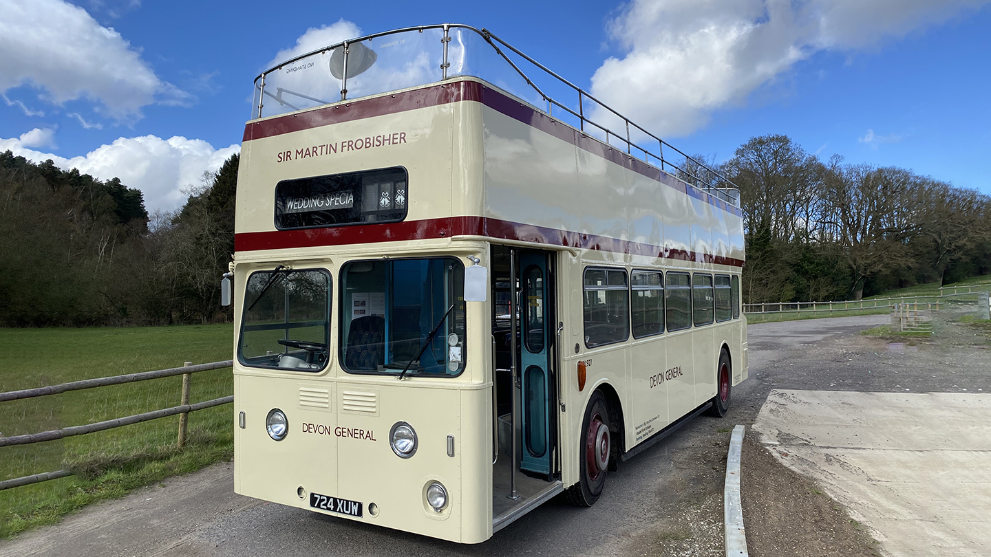 Cream vintage Leyland double decker bus parked beside farmland and countryside scenery.