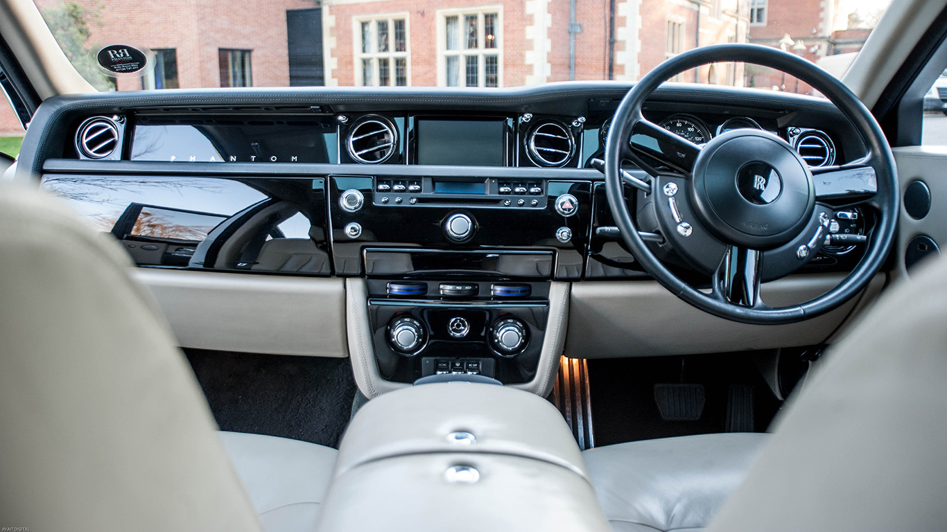 Front interior of a white Rolls-Royce Phantom showing cream leather seats, luxury dashboard controls and polished interior trim.