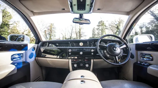 Driver view of Rolls-Royce Phantom interior with cream leather dashboard, polished wood trim and luxury instrument panel.