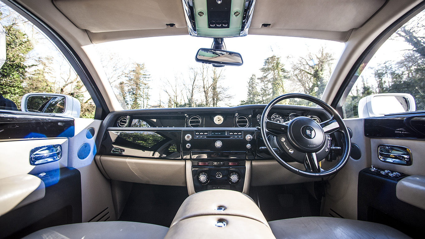 Driver view of Rolls-Royce Phantom interior with cream leather dashboard, polished wood trim and luxury instrument panel.