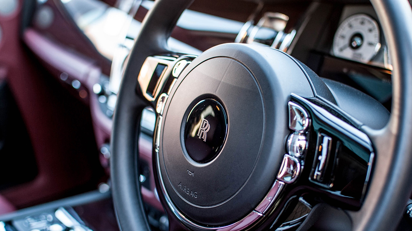 Close view of Rolls-Royce Ghost driver dashboard with leather steering wheel, chrome controls, luxury instrument cluster and polished interior trim.
