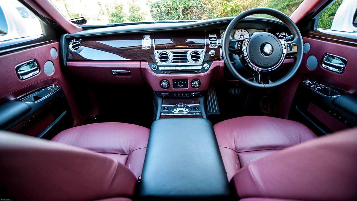 Front interior seats of Rolls-Royce Ghost luxury car with burgundy leather seating, centre console and polished dashboard trim.
