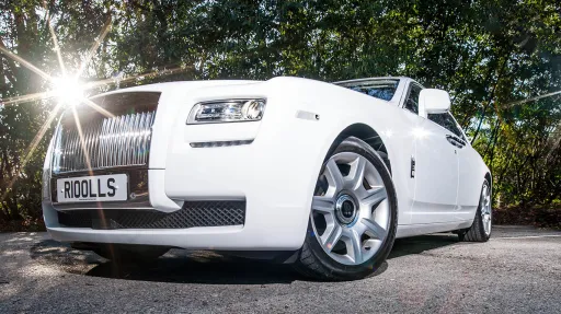 Front left view of a white Rolls-Royce Ghost wedding car featuring the iconic chrome radiator grille, Spirit of Ecstasy bonnet ornament and polished alloy wheels parked outdoors.