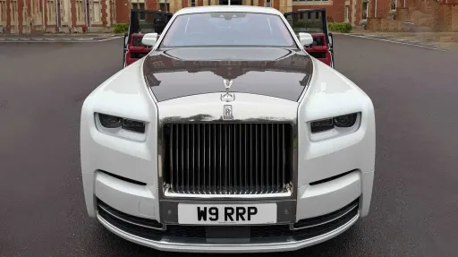 Front view of a white Rolls-Royce Phantom VIII luxury wedding car with grey bonnet, polished chrome grille, Spirit of Ecstasy bonnet ornament parked on a road.