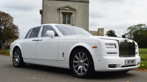White Rolls-Royce Phantom Series II luxury chauffeur driven wedding car with polished chrome grille and alloy wheels parked outside a historic building.