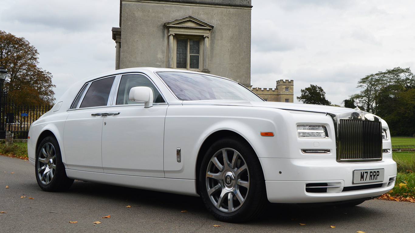 White Rolls-Royce Phantom Series II luxury chauffeur driven wedding car with polished chrome grille and alloy wheels parked outside a historic building.