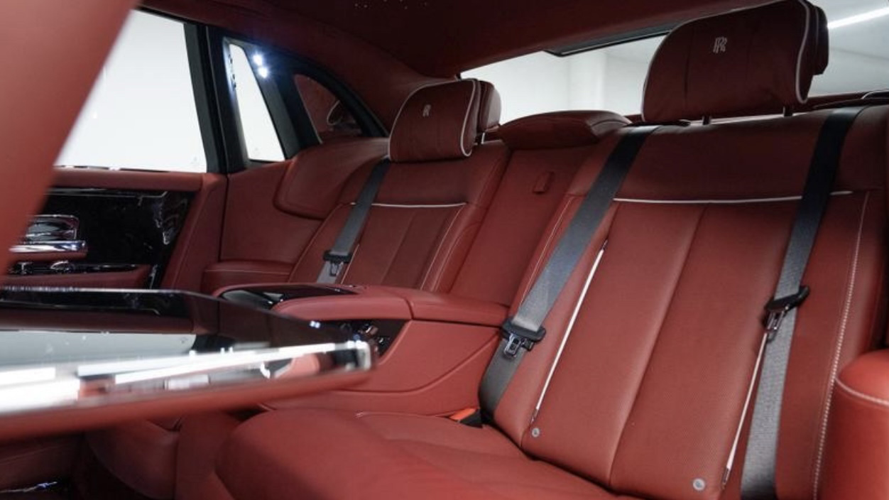 Rear passenger seating inside Rolls-Royce Phantom VIII featuring red leather seats, centre armrest and luxury handcrafted interior trim.