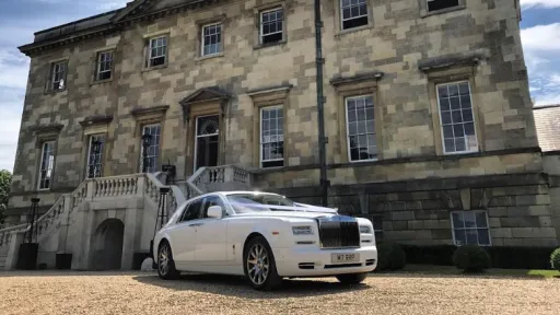 White Rolls-Royce Phantom Series II EWB luxury wedding car with polished chrome grille and alloy wheels parked outside a historic stone wedding venue.