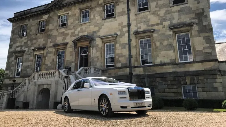 White Rolls-Royce Phantom Series II EWB luxury wedding car with polished chrome grille and alloy wheels parked outside a historic stone wedding venue.