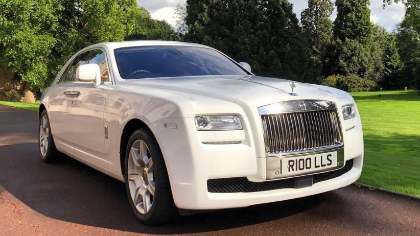White Rolls-Royce Ghost luxury wedding car with polished chrome grille, Spirit of Ecstasy bonnet ornament and alloy wheels photographed on a driveway beside green lawns.