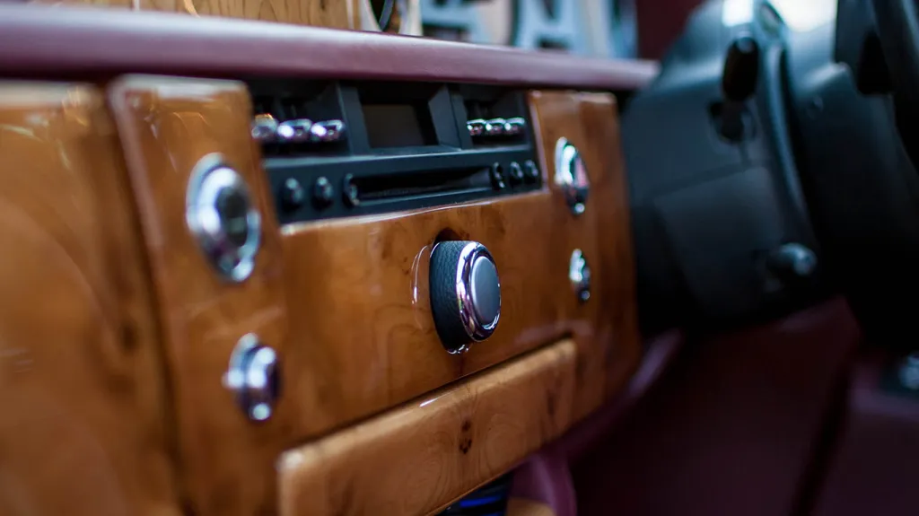 Front dashboard inside Rolls-Royce Phantom showing polished wood veneer trim, chrome controls and luxury interior detailing.
