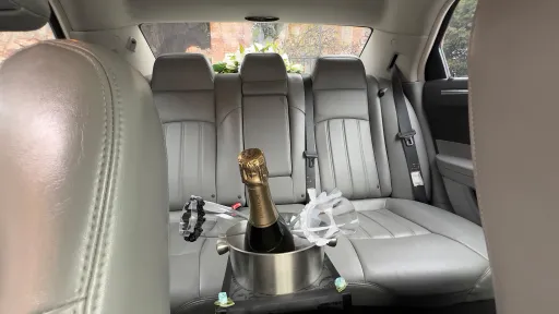 Rear interior of a Chrysler 300C wedding car showing light silver leather seats with champagne bottle and glasses placed between the rear seats.