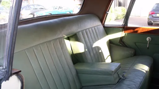 Interior view showing sage green leather seats inside vintage car, door panel and stitching visible.