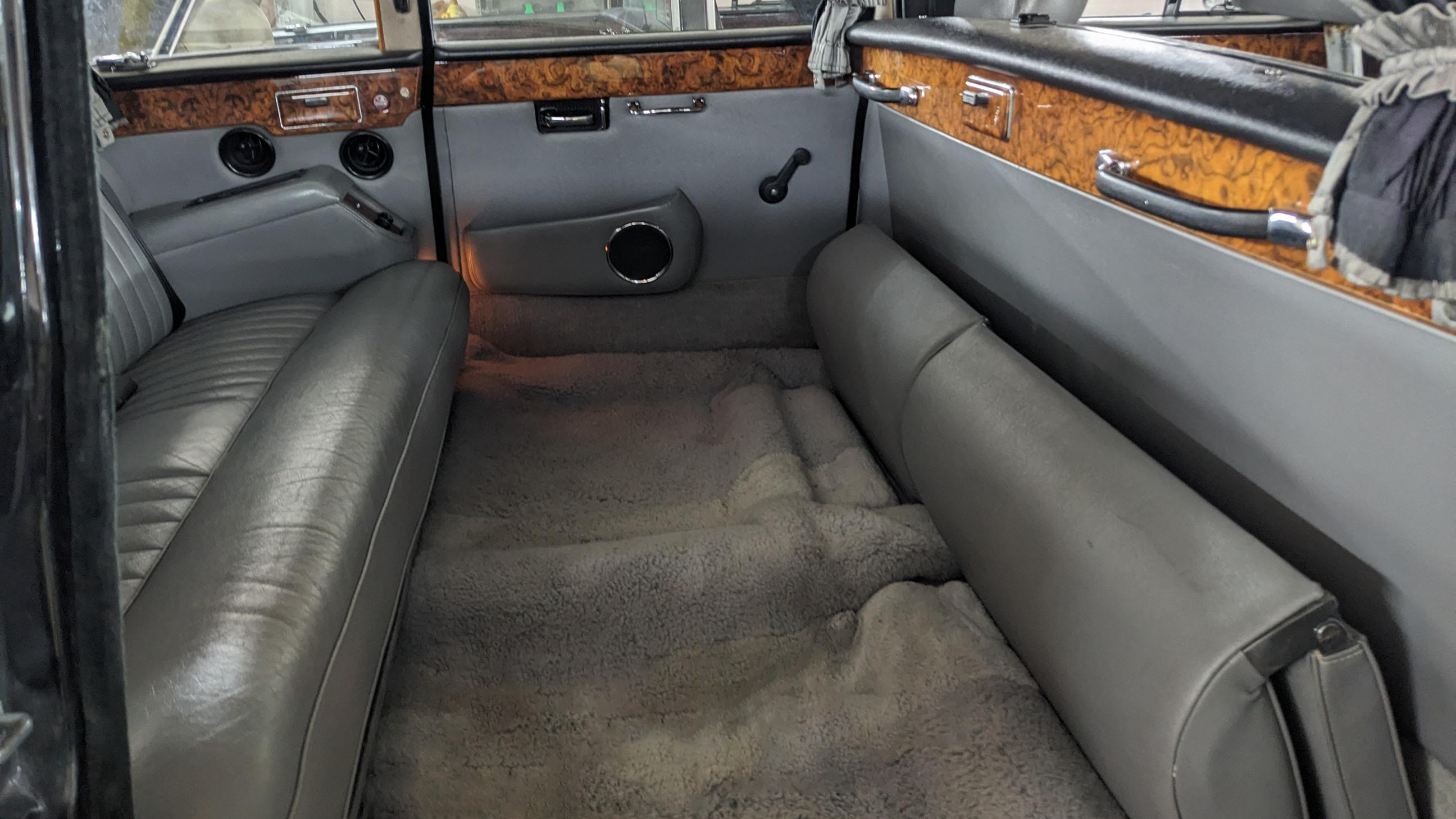 Spacious rear compartment of Daimler DS420 limousine showing extended legroom area between bench seats, grey leather seating on both sides, wood veneer panels and clean carpeted floor.