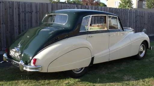 Rear left view of Armstrong Siddeley with green roof and ivory body, parked on grass with wooden fence behind.