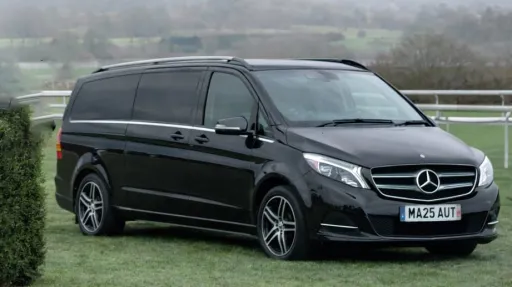 Black Mercedes V-Class AMG with cream leather interior, parked on roadside with countryside hills in background.