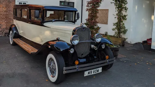 Front angle view of black and ivory Bramwith limousine with chrome grille and white wall tyres, parked outside building.