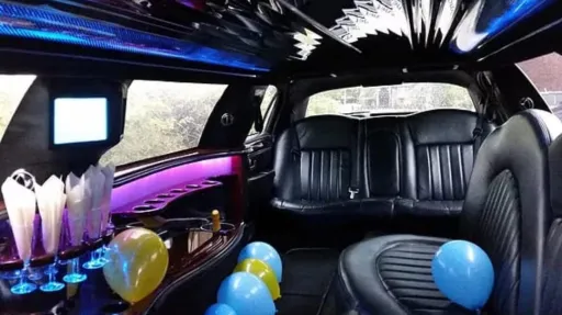 Interior of Lincoln stretch limousine with black leather seating, LED lighting, drinks area and party-style cabin setup with blue and yellow ballons