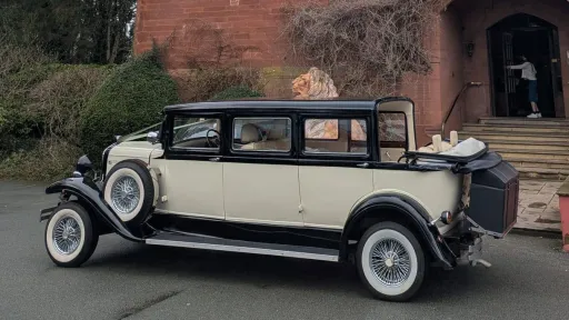 Black and ivory Bramwith Landaulette limousine with cream interior, side view on road with village houses in background.