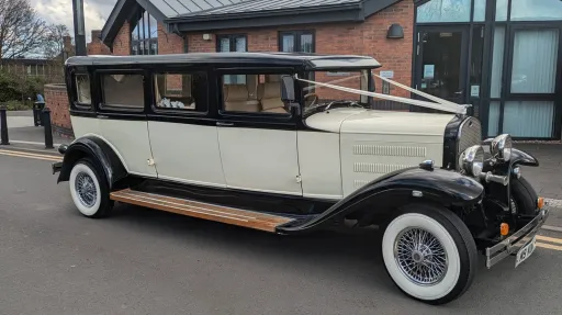 Side profile of black and ivory Bramwith limousine parked on road, showing long body and classic vintage styling.