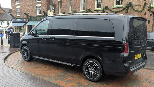 Rear left angle of black Mercedes V-Class AMG parked on cobbled street, urban buildings in background.