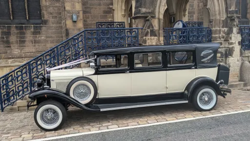 Left side view of black and ivory Bramwith Landaulette limousine, parked near stone steps with historic building behind.