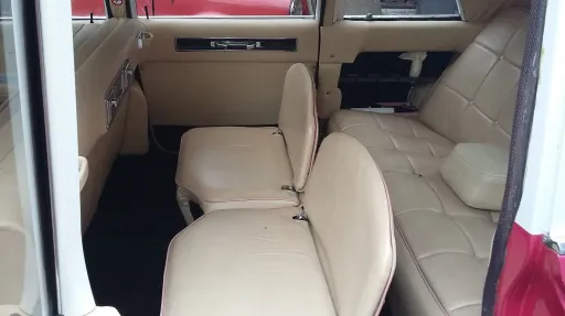 Rear cabin of Cadillac limousine with cream leather seats, showing spacious bench seating and interior layout.