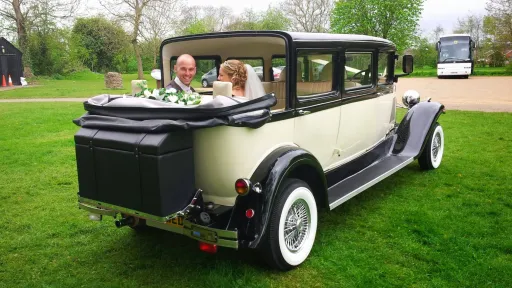Rear view of Bramwith Landaulette with roof open, bride and groom seated inside, parked on grass with trees around.
