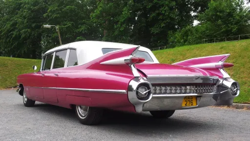Close rear view of pink Cadillac Fleetwood limousine highlighting chrome bumper and large tail fins.