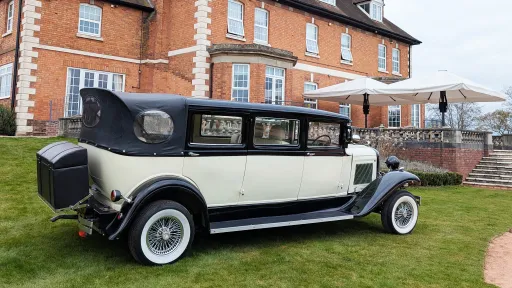 Right side view of Bramwith Landaulette limousine in black and ivory, parked on grass outside large house.