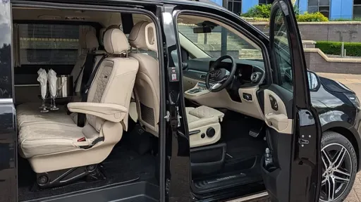 Black Mercedes V-Class AMG with sliding door open, showing cream leather interior and captain seats, parked outside modern building.