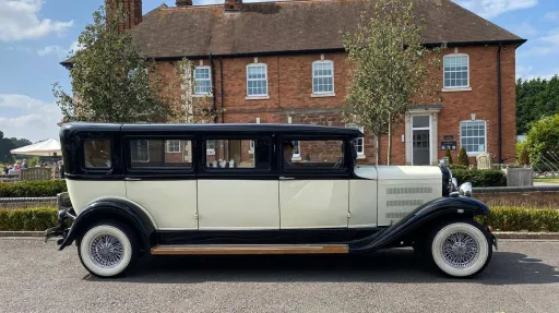 Right side view of black and ivory Bramwith limousine parked outside brick house, full length profile visible.
