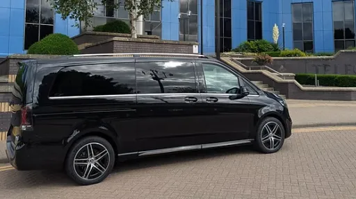 Black Mercedes V-Class AMG with tinted privacy windows, side profile parked on driveway outside modern building.