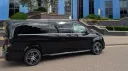 Black Mercedes V-Class AMG with tinted privacy windows, side profile parked on driveway outside modern building.