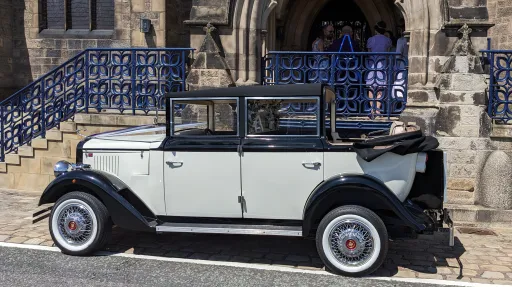 Left side view of Cowley landaulette limousine with rear roof open, black and ivory coachwork, and white wall tyres.
