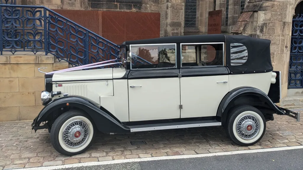 Black and ivory Cowley limousine with landaulette roof closed, full side profile with cream panels and white wall tyres.