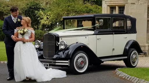 Black and ivory Cowley vintage limousine parked on grass with bride and groom, landaulette roof closed, classic styling and chrome details.