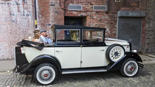 Cowley landaulette limousine with rear roof open, couple seated inside, showing picnic trunk, side spare wheel and vintage styling.