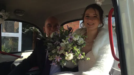 Bride and her father seated inside a classic taxi cab, burgundy leather interior visible with natural light through the side window.