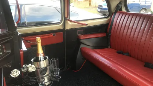 Interior of a classic FX4 taxi cab showing burgundy leather bench seating and traditional cabin layout with drinks hold