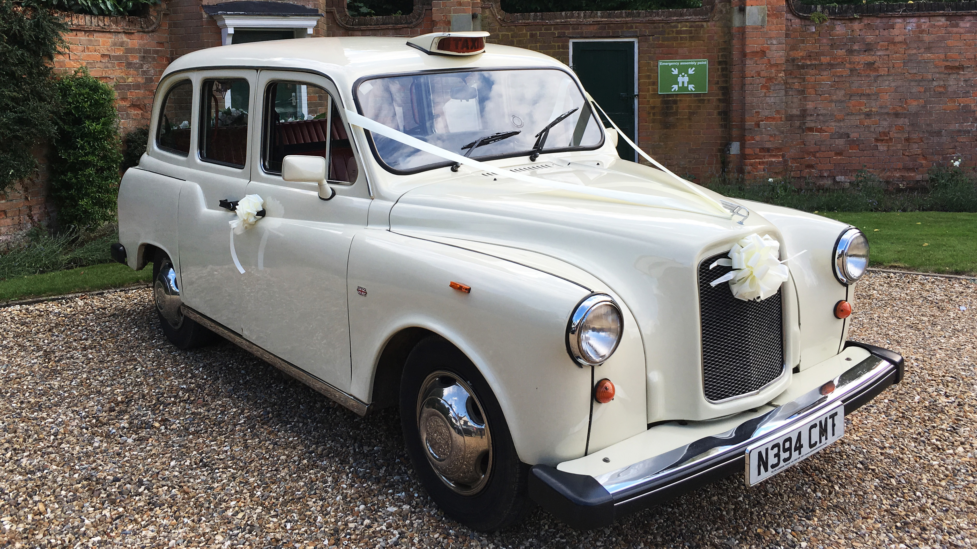 Old English White classic taxi cab parked on a gravel drive, front angle showing chrome grille and classic styling.