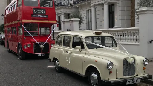 Classic ivory taxi cab parked alongside a red vintage Routemaster bus, outdoor setting with building in background.