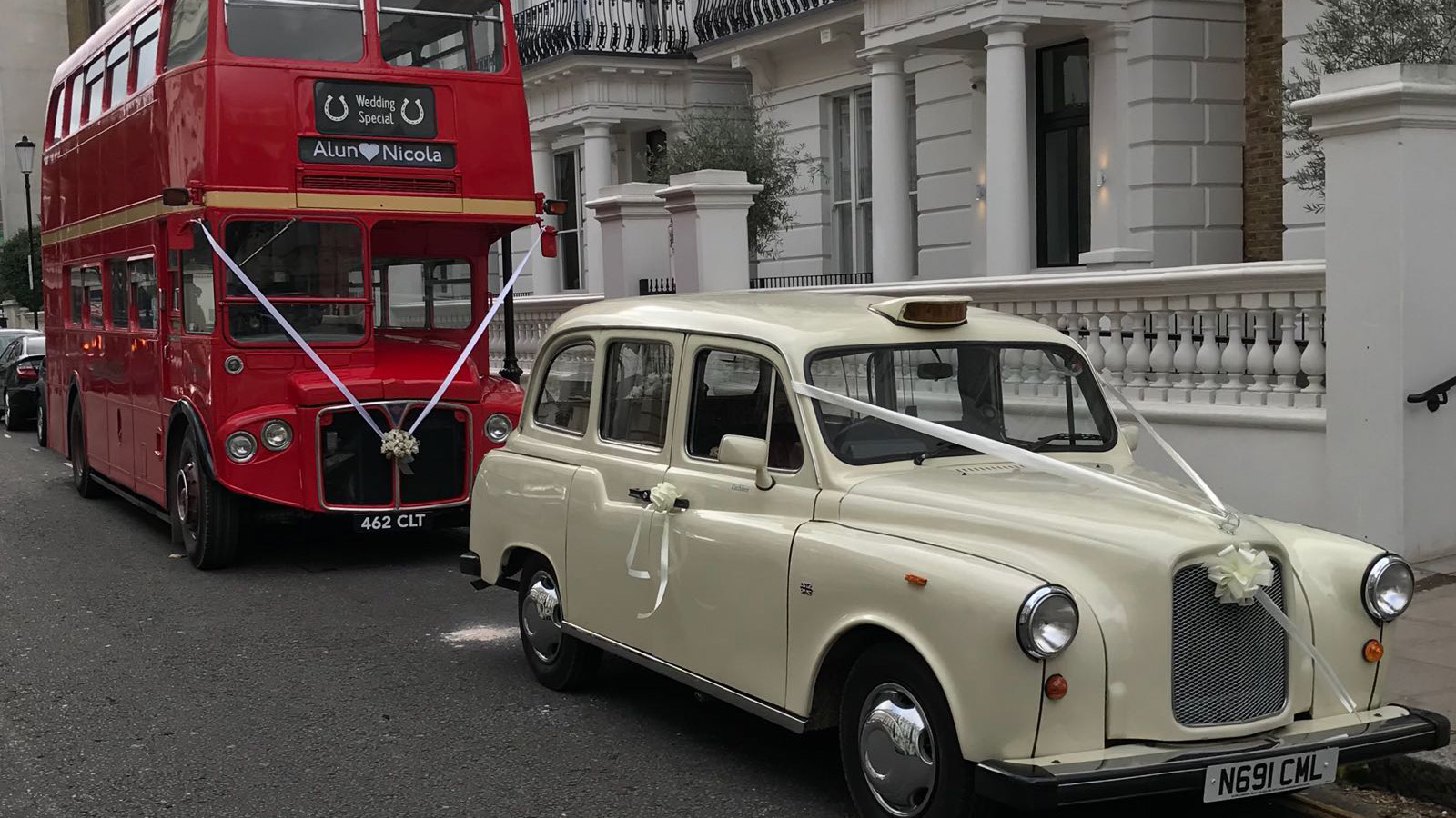 Classic ivory taxi cab parked alongside a red vintage Routemaster bus, outdoor setting with building in background.