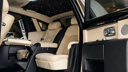 Interior of a Rolls-Royce Phantom featuring cream leather seats and illuminated starlight headliner, rear cabin view.
