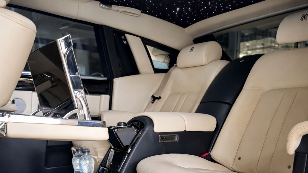 Rear interior of a Rolls-Royce Phantom with cream leather seating, centre armrest and luxury cabin finish.