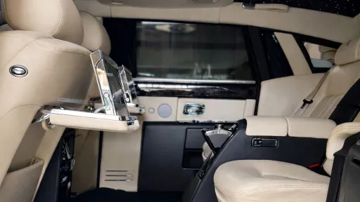 Rear seating area of a Rolls-Royce Phantom with two individual cream leather seats separated by a fixed centre armrest.