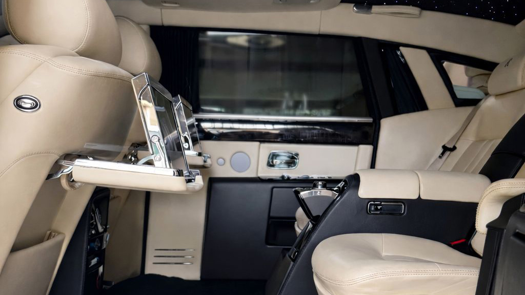 Rear seating area of a Rolls-Royce Phantom with two individual cream leather seats separated by a fixed centre armrest.