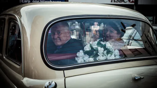 Rear window view of passengers seated inside a classic taxi cab, burgundy leather interior visible with natural light entering the cabin.